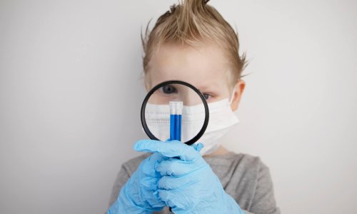 The child plays a doctor and a scientist. A boy in a medical mask studies a medicine in a test tube through a magnifying glass. The concept of education and promotion of medical professions